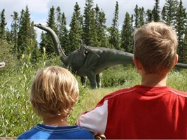 2 kids looking at a dinosaur in a field